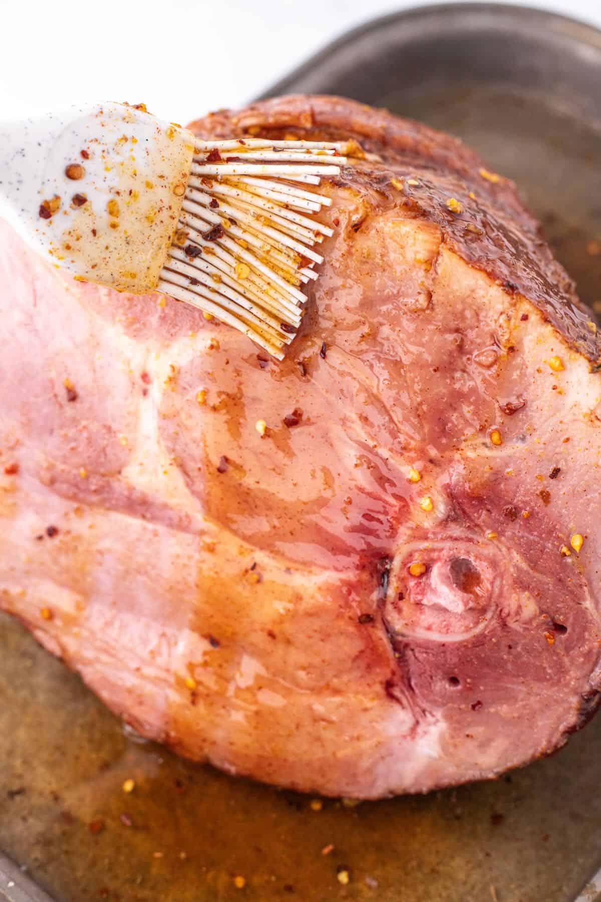 Using a pastry brush to add a spicy maple glaze to a whole ham.