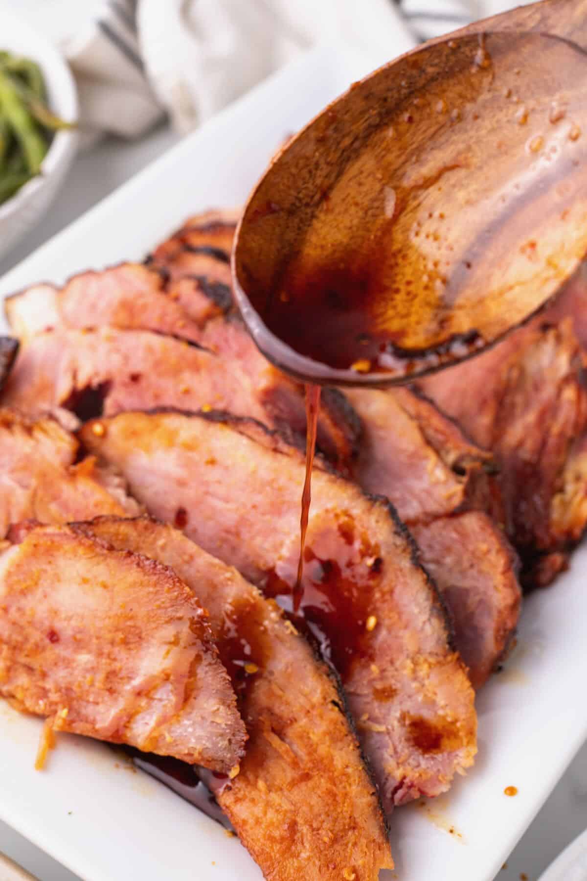 Slices of maple glazed ham with glaze being spooned over the top of them. 