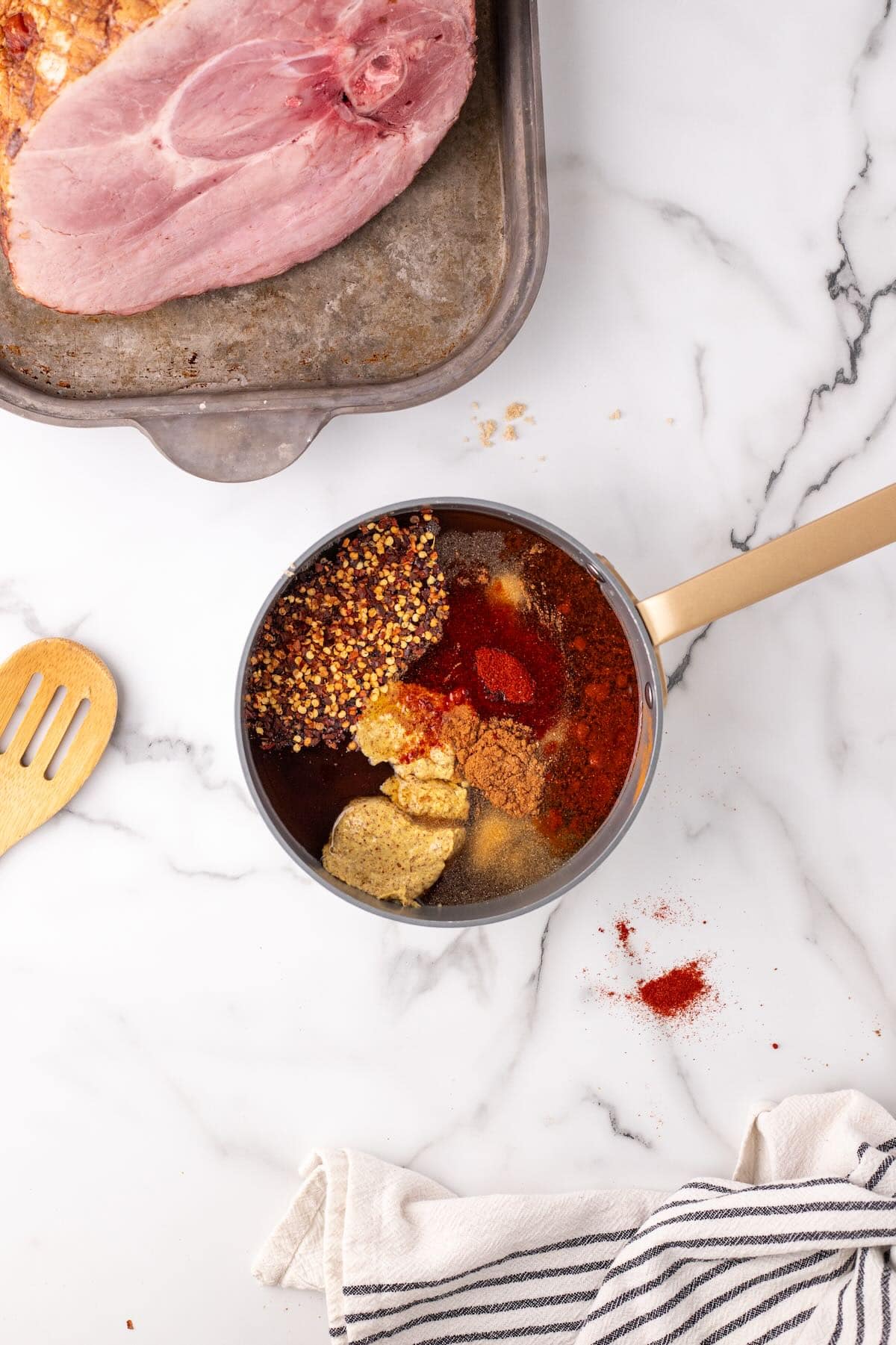 Ingredients for making a ham glaze in a saucepan include honey, maple syrup, and brown sugar. 
