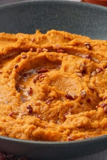 A large gray bowl full of savory mashed sweet potatoes with brown butter swirled around, topped with candied nuts.