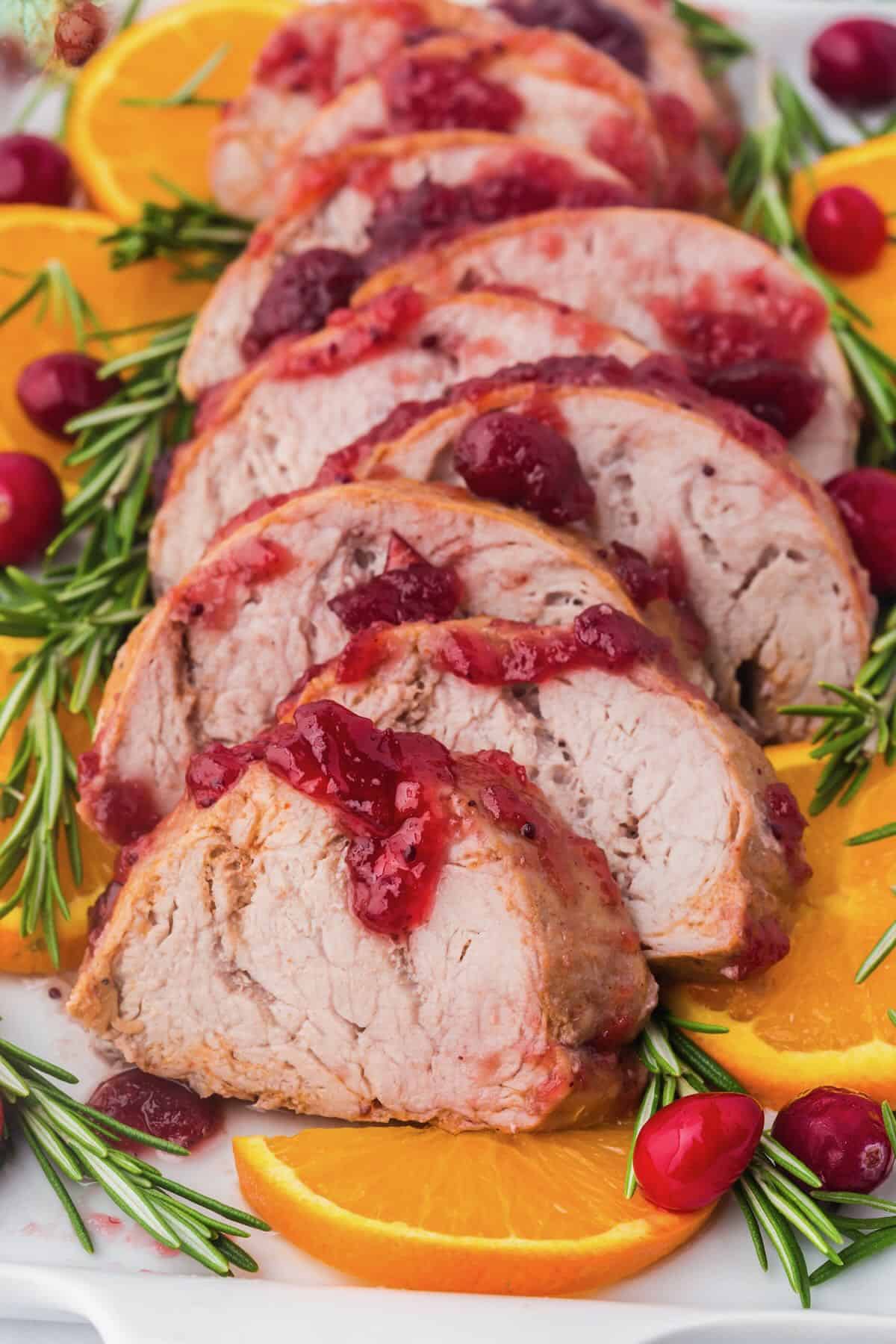 Cooked rosemary pork tenderloin sliced and topped with cranberry sauce and rosemary. 