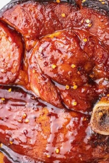 A whole bone-in spicy maple glazed ham in a baking pan.