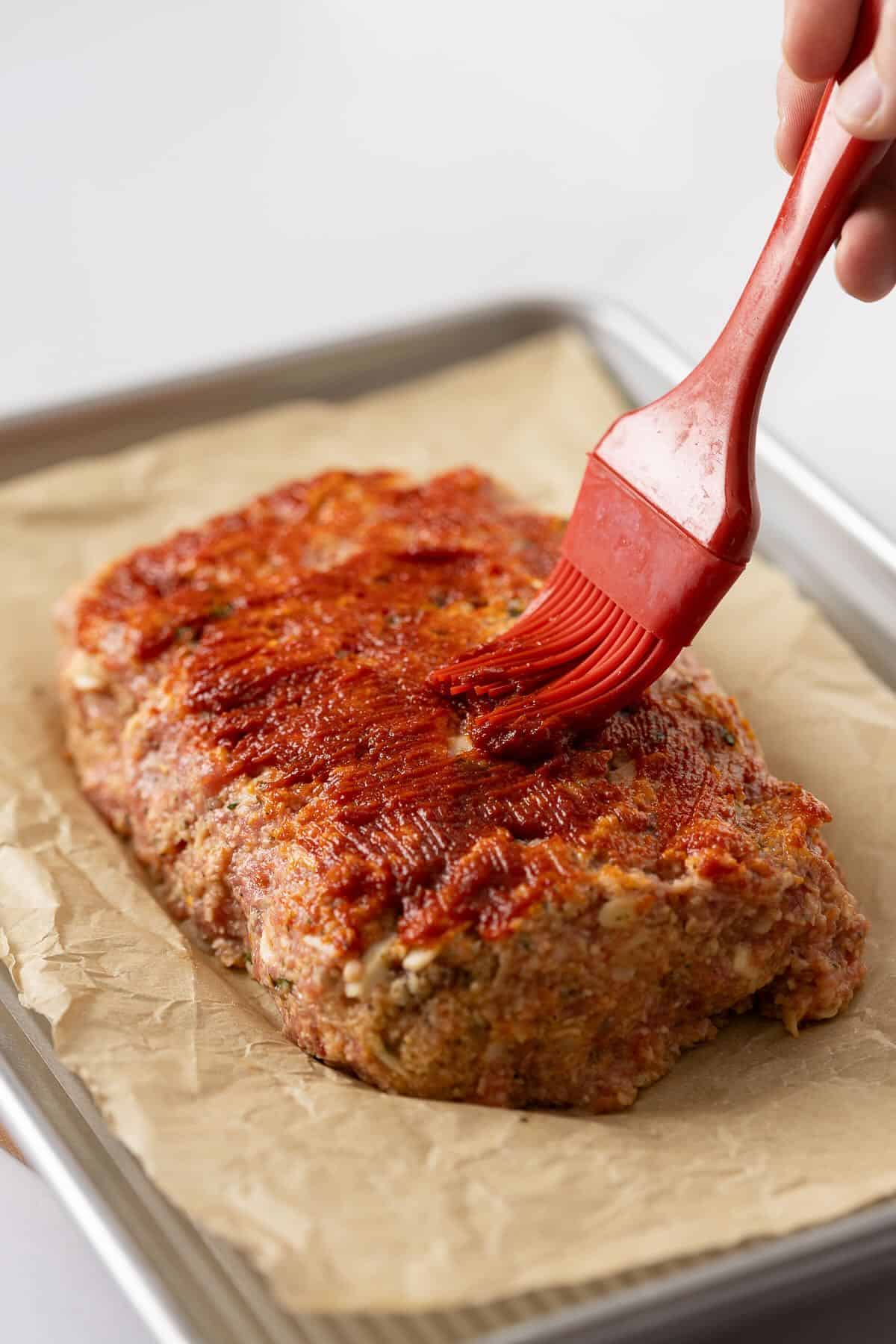 Using a pastry brush to add a tomato based glaze to an unbaked meatloaf.
