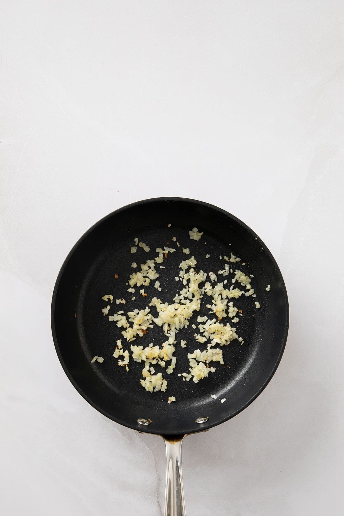 Chopped shallots and garlic are cooking in a skillet.