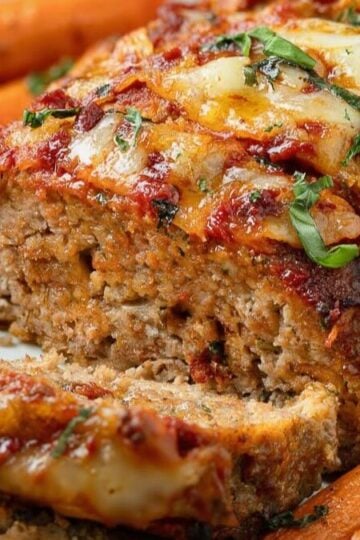 A 1-pound Meatloaf cut into slices on a cutting board with roasted carrots on the side.