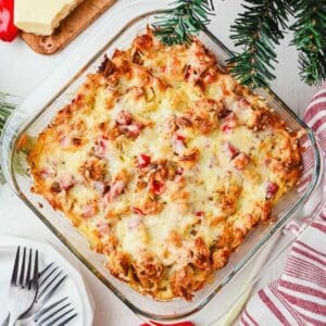 A baked make-ahead croissant breakfast casserole with ham on a table with plates and forks.