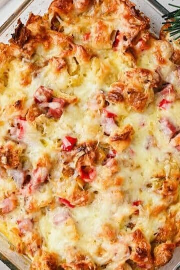 A baked make-ahead croissant breakfast casserole with ham on a table with plates and forks.