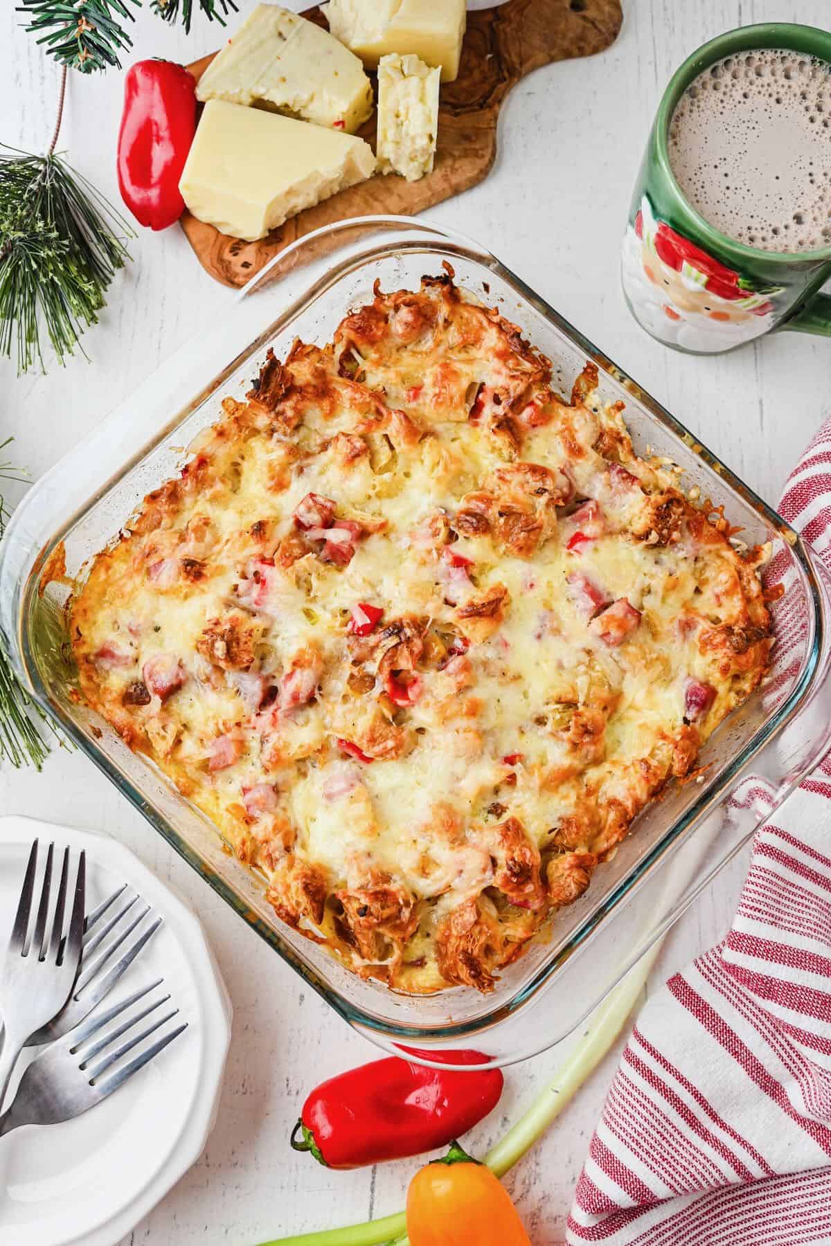 A baked croissant breakfast casserole on a table with a red and white napkin and plate and forks.