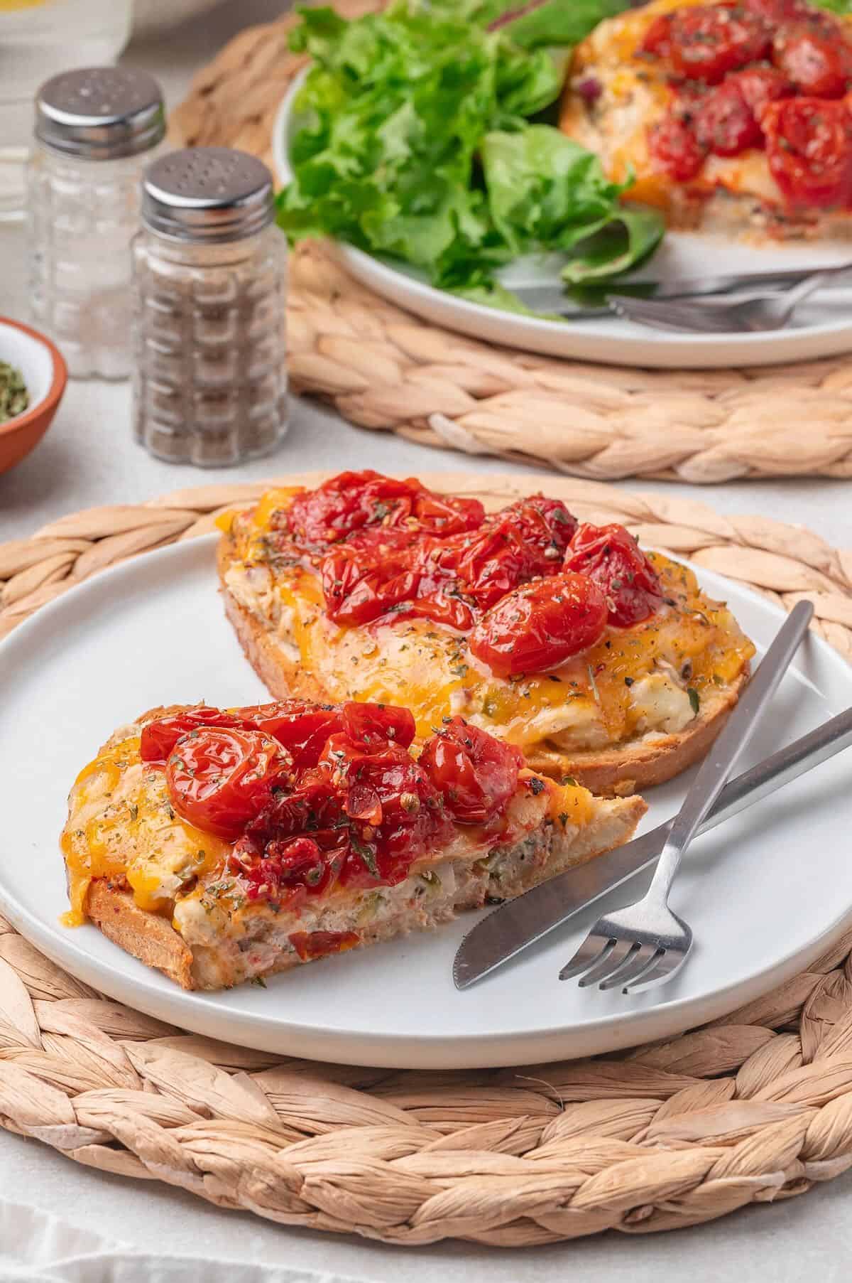 Open face tuna melts on a plate topped with melted cheese and cherry tomatoes. 