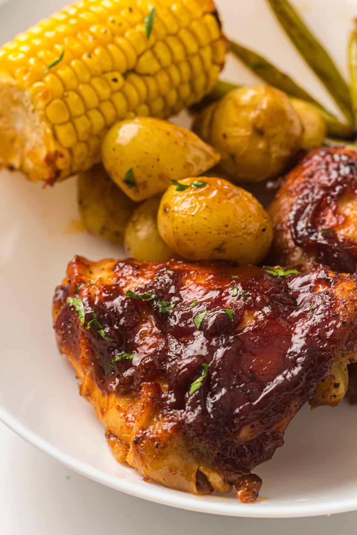 Sheet Pan BBQ Chicken plated with potatoes, corn, and green beans. 