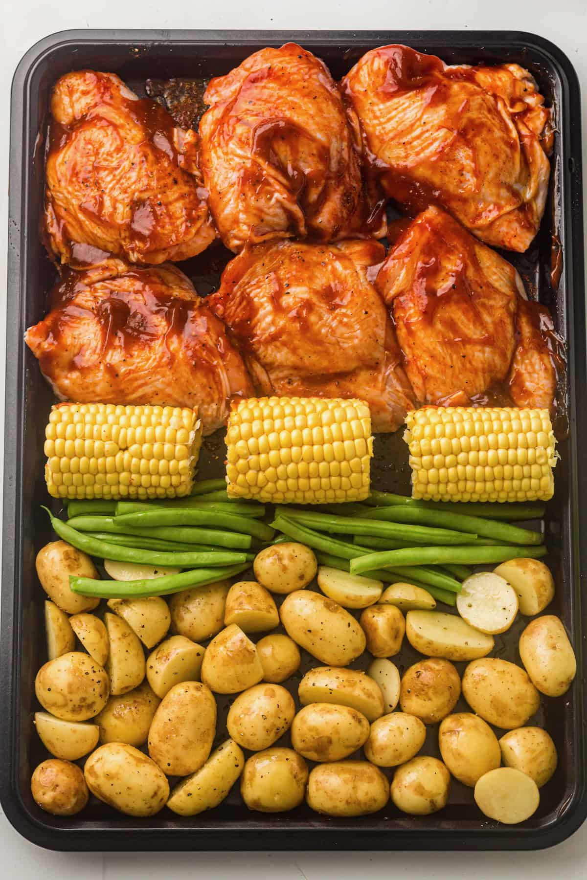 Chicken thighs, corn, green beans and corn on a sheet pan ready to cook.
