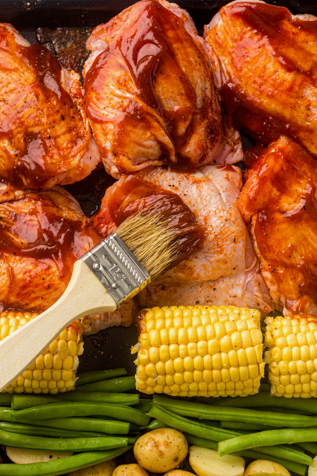 Using a pastry brush to apply BBQ sauce to chicken thighs.